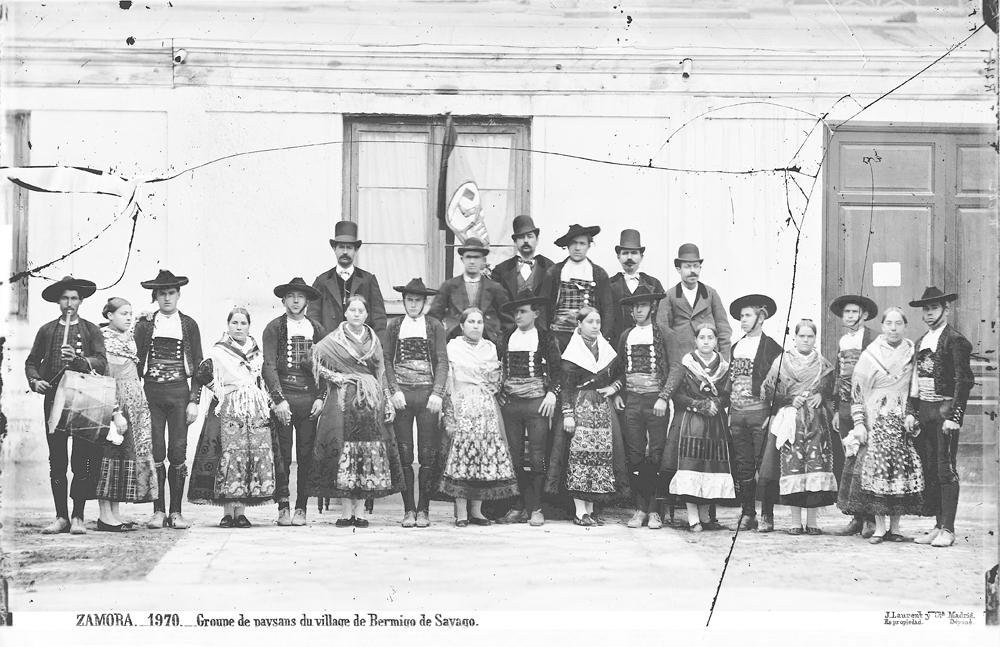Fotografía antigua en blanco y negro de un grupo de hombres y mujeres de Bermillo de Sayago con el traje tradicional, delante de una fachada